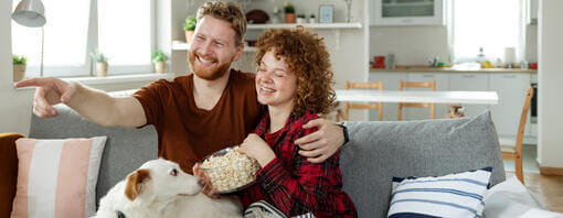Couple and dog on a sofa with a bowl of popcorn